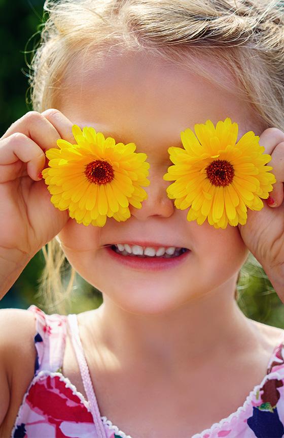 Smiling child holding flowers up to her eyes
